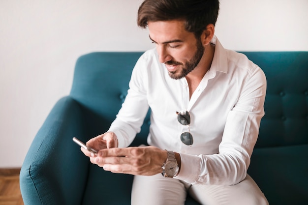 Hombre sentado en el sofá usando teléfono móvil