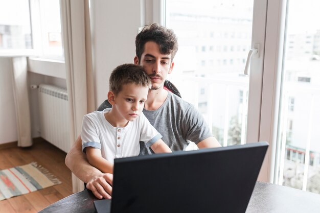 Hombre sentado con su hijo usando laptop