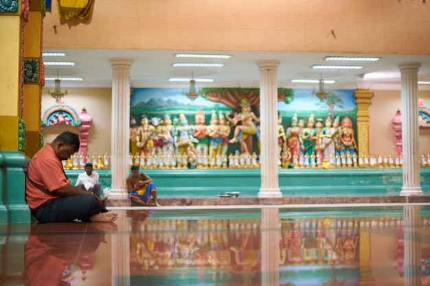 Hombre sentado en el suelo delante de un templo con estatuas