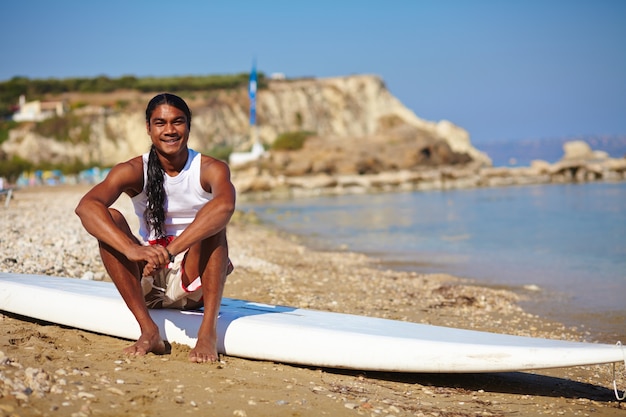 Hombre sentado en una tabla de surf en la orilla de la playa