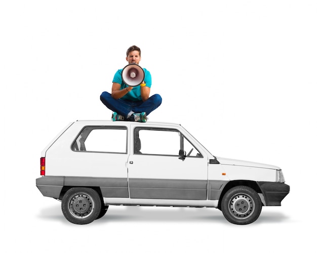 Hombre sentado en el techo de un coche con un megáfono gritando