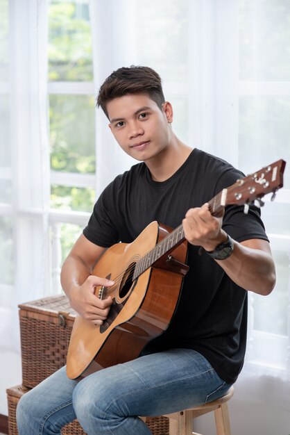 Un hombre sentado y tocando la guitarra en una silla.