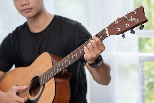 Un hombre sentado y tocando la guitarra en una silla.