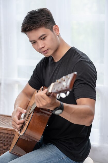 Un hombre sentado y tocando la guitarra en una silla.