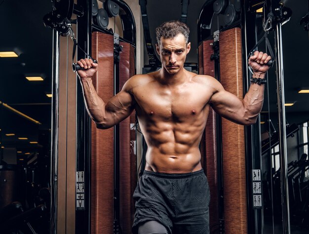 Un hombre serio y atractivo está haciendo ejercicios con aparatos de entrenamiento en un club de gimnasia oscuro.