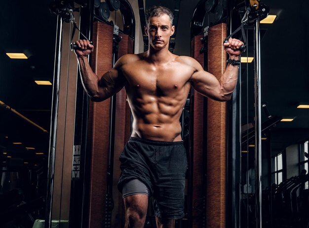 Un hombre serio y atractivo está haciendo ejercicios con aparatos de entrenamiento en un club de gimnasia oscuro.