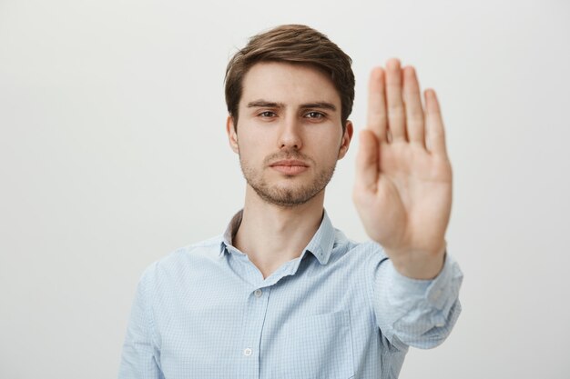 Hombre serio confiado extiende la mano para detener la tienda, advertencia o restricción