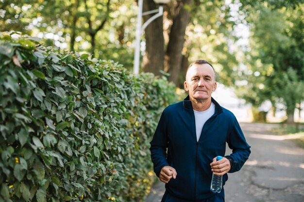 Foto gratuita hombre serio corriendo con una botella de agua en la mano