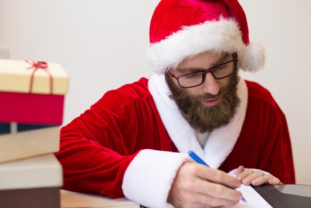 Hombre serio disfrazado de santa y trabajando con documentos.