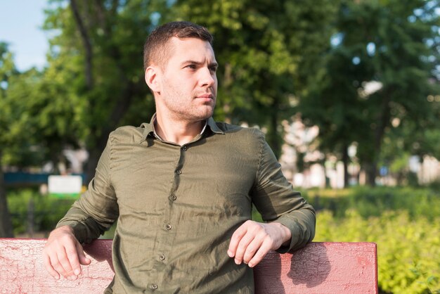 Hombre serio joven que se sienta en banco en parque