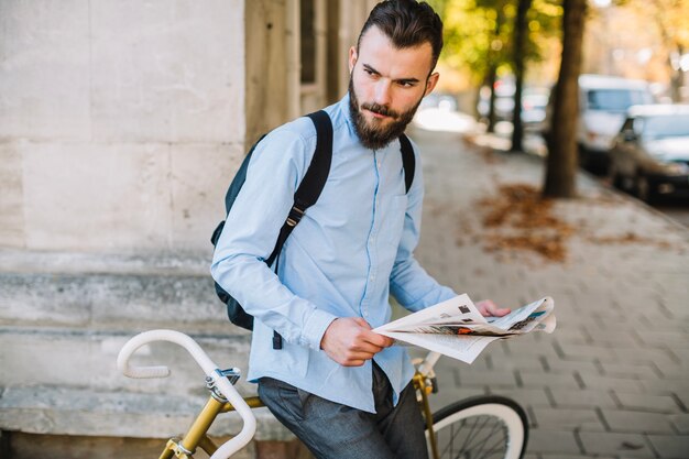 Hombre serio con periódico cerca de bicicleta