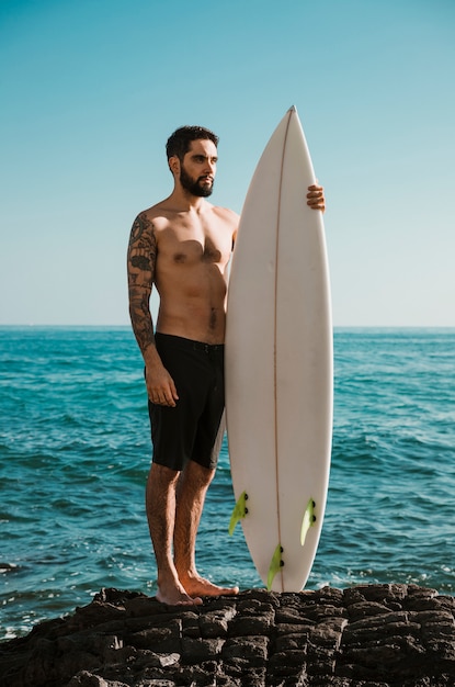 Hombre serio con pie de tabla de surf en roca