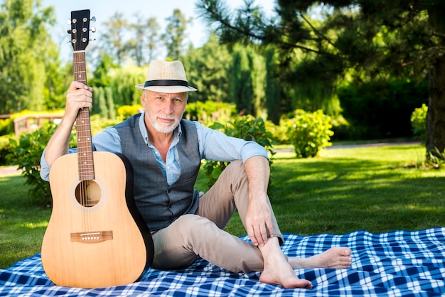 Foto gratuita hombre serio que sostiene una guitarra en la naturaleza