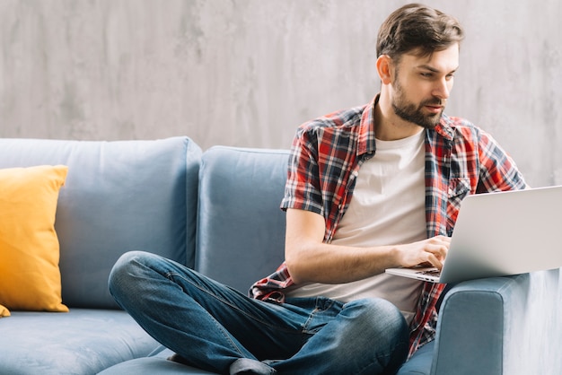 Hombre serio que usa la computadora portátil en el sofá