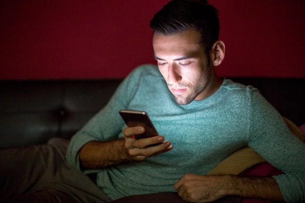 Foto gratuita hombre serio que usa el teléfono inteligente en el sofá en la noche