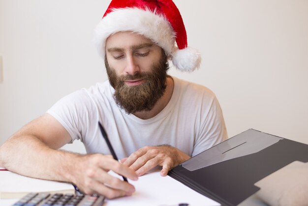 Hombre serio con sombrero de Santa y trabajando con documentos