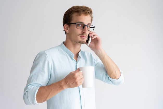 Hombre serio sosteniendo la taza y hablando por teléfono inteligente