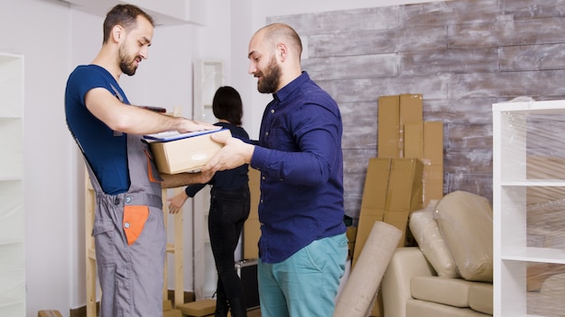 Hombre del servicio de entrega que llega con cajas y documentos a firmar. Hermosa joven pareja entrando.