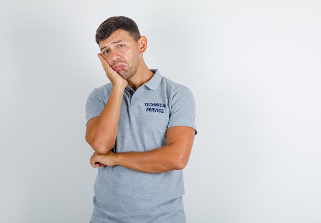 Hombre de servicio técnico apoyando su mejilla en la palma levantada en camiseta gris y mirando molesto