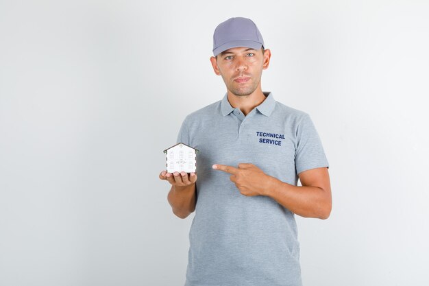 Hombre de servicio técnico en camiseta gris con gorra que muestra el modelo de la casa con el dedo