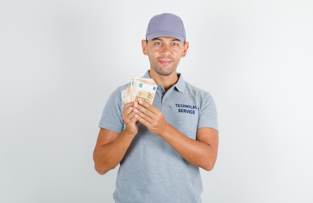 Hombre de servicio técnico en camiseta gris con gorra sosteniendo billetes en euros