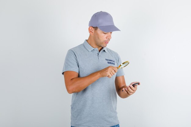 Hombre de servicio técnico mirando smartphone con lupa en camiseta gris con gorra