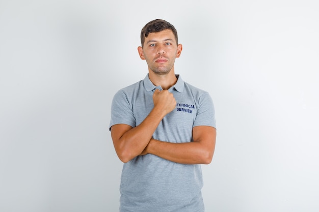 Hombre de servicio técnico de pie con el puño cerrado en camiseta gris y mirando serio