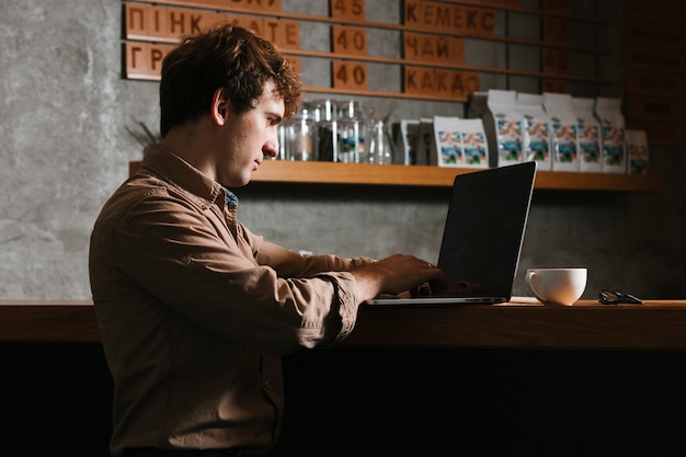 Hombre de Sideview que trabaja en la computadora portátil en la oficina