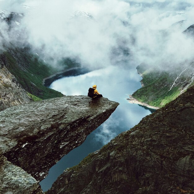 El hombre se sienta en el extremo de Trolltunga antes de las montañas
