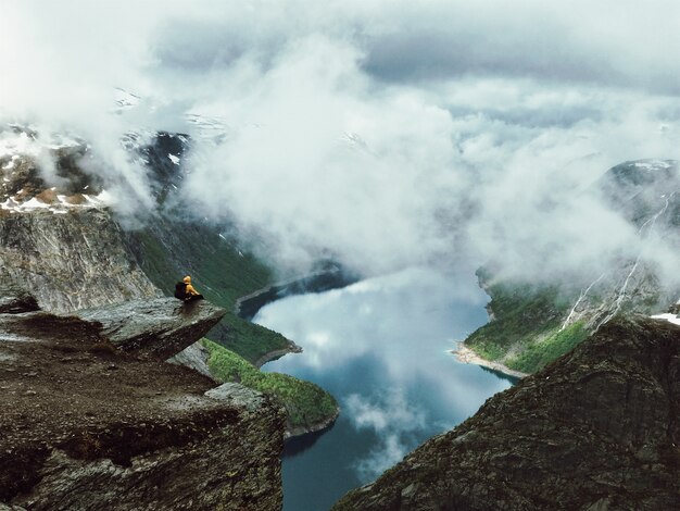 El hombre se sienta en el extremo de Trolltunga antes de las montañas