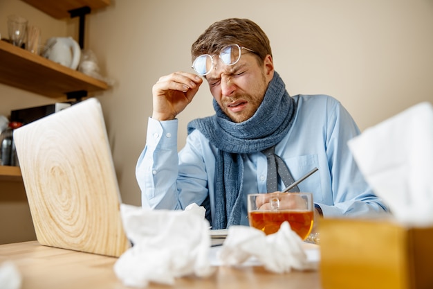 El hombre se siente enfermo y cansado. hombre con taza trabajando en casa, empresario resfriado, gripe estacional.