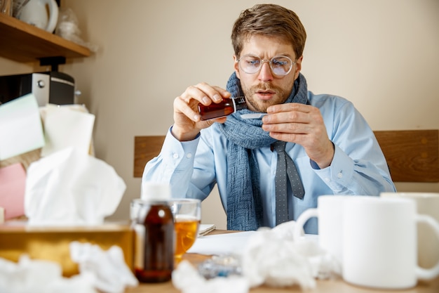 El hombre se siente enfermo y cansado. hombre con taza trabajando en casa, empresario resfriado, gripe estacional.