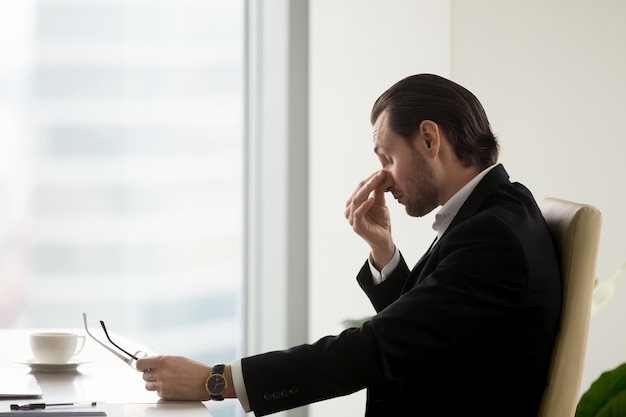 El hombre siente fatiga en los ojos después de trabajar en la oficina