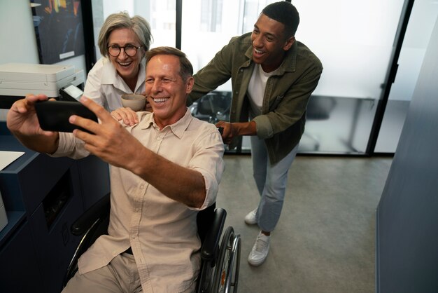Hombre en silla de ruedas tomándose un selfie en su lugar de trabajo con colegas