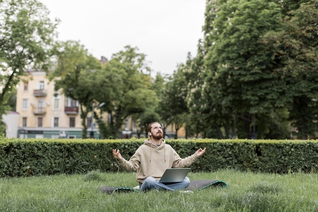 Foto gratuita hombre sintiendo zen en el parque de la ciudad con laptop