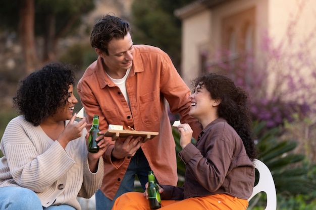 Hombre sirviendo un plato de queso a sus amigas durante una fiesta al aire libre