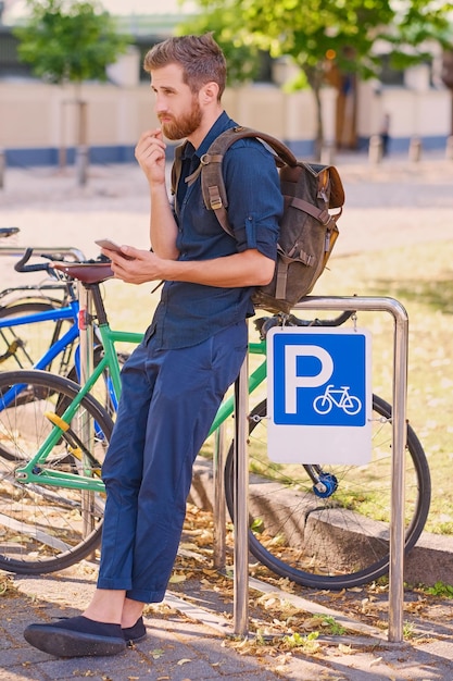 Un hombre con smartphone cerca del área de estacionamiento de bicicletas.