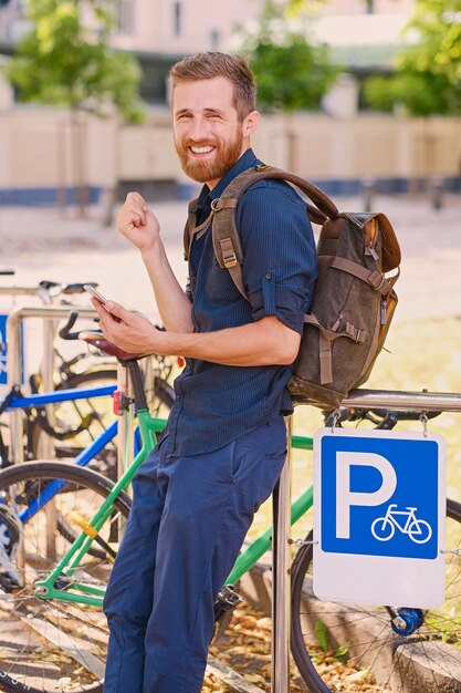 Un hombre con smartphone cerca del área de estacionamiento de bicicletas.