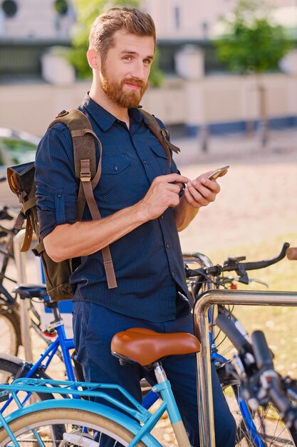 Un hombre con smartphone cerca del área de estacionamiento de bicicletas.