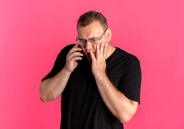 Hombre con sobrepeso en gafas vistiendo camiseta negra hablando por teléfono móvil siendo sorprendido por rosa