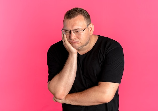 Foto gratuita hombre con sobrepeso en gafas vistiendo camiseta negra molesto apoyando la cabeza en el brazo esperando rosa