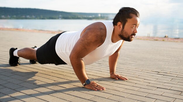 Hombre con sobrepeso haciendo flexiones en el muelle al aire libre