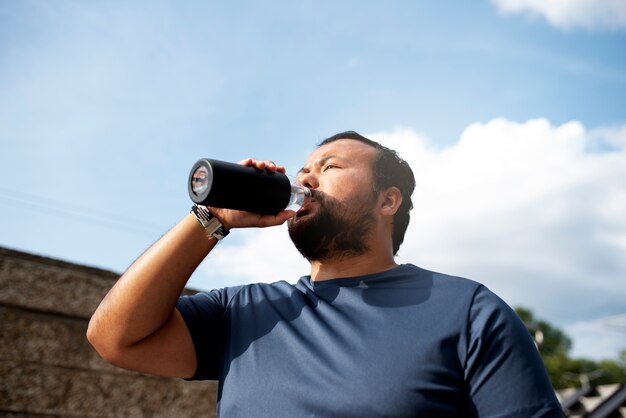 Hombre con sobrepeso hidratándose con agua después de hacer ejercicio