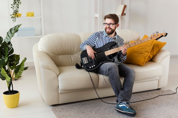 Hombre en el sofá en casa tocando la guitarra eléctrica