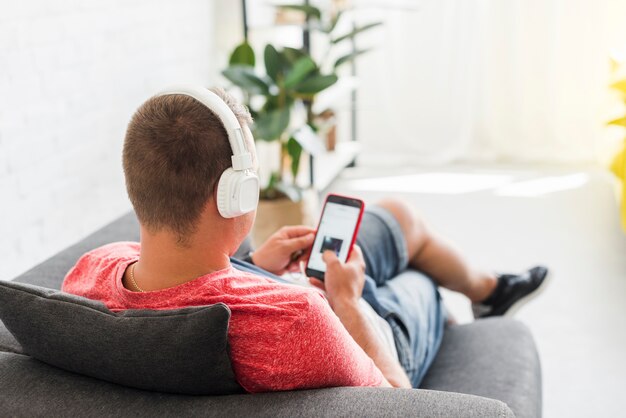 Hombre en el sofá ve una película en el teléfono móvil con auriculares