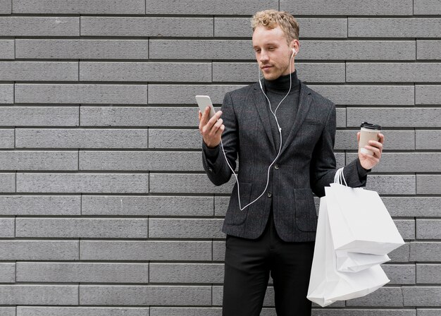 Hombre solitario con bolsas de compras sonriendo al teléfono inteligente