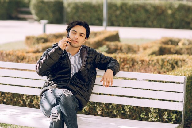 Hombre soltero sentado en el banco en el parque y hablando por teléfono. Foto de alta calidad