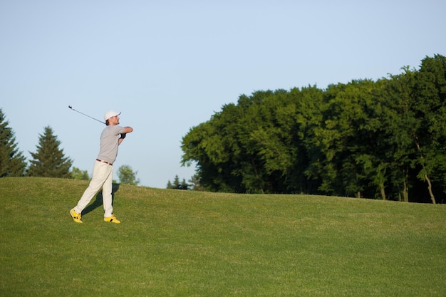 Hombre con sombrero jugando al golf profesional en el aire. Golfista golpeando un tiro de golf con un palo en el campo.