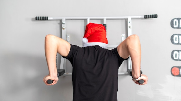 Un hombre con sombrero de navidad en las barras asimétricas en un gimnasio. Vista trasera