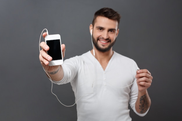 Hombre sonriendo estirando la pantalla del teléfono sobre la pared gris